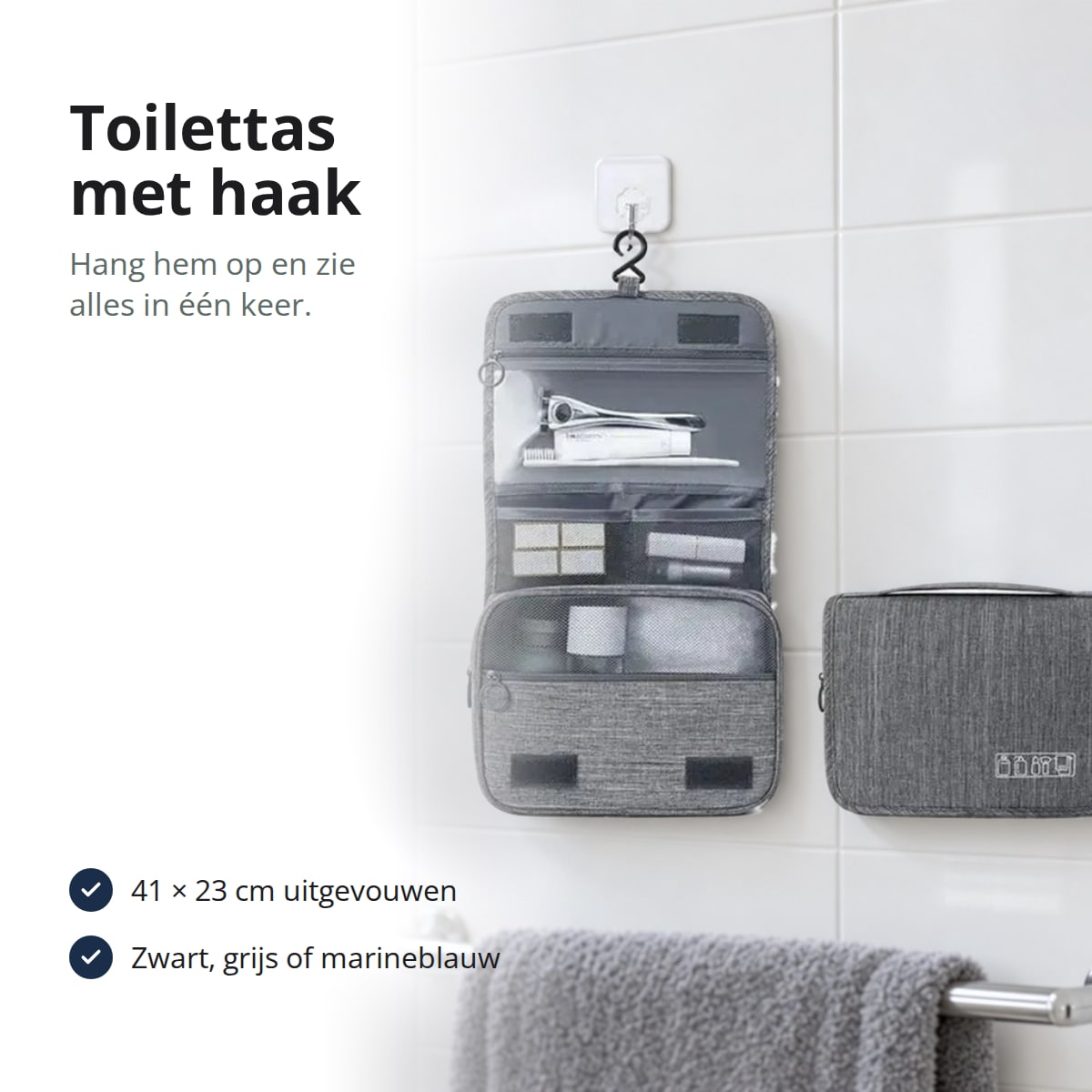 Grijze toilettas met haak, uitgevouwen en dicht, opgehangen aan een witte tegelwand boven een handdoekstang, met de tekst: 41 × 23 cm uitgevouwen, zwart, grijs of marineblauw