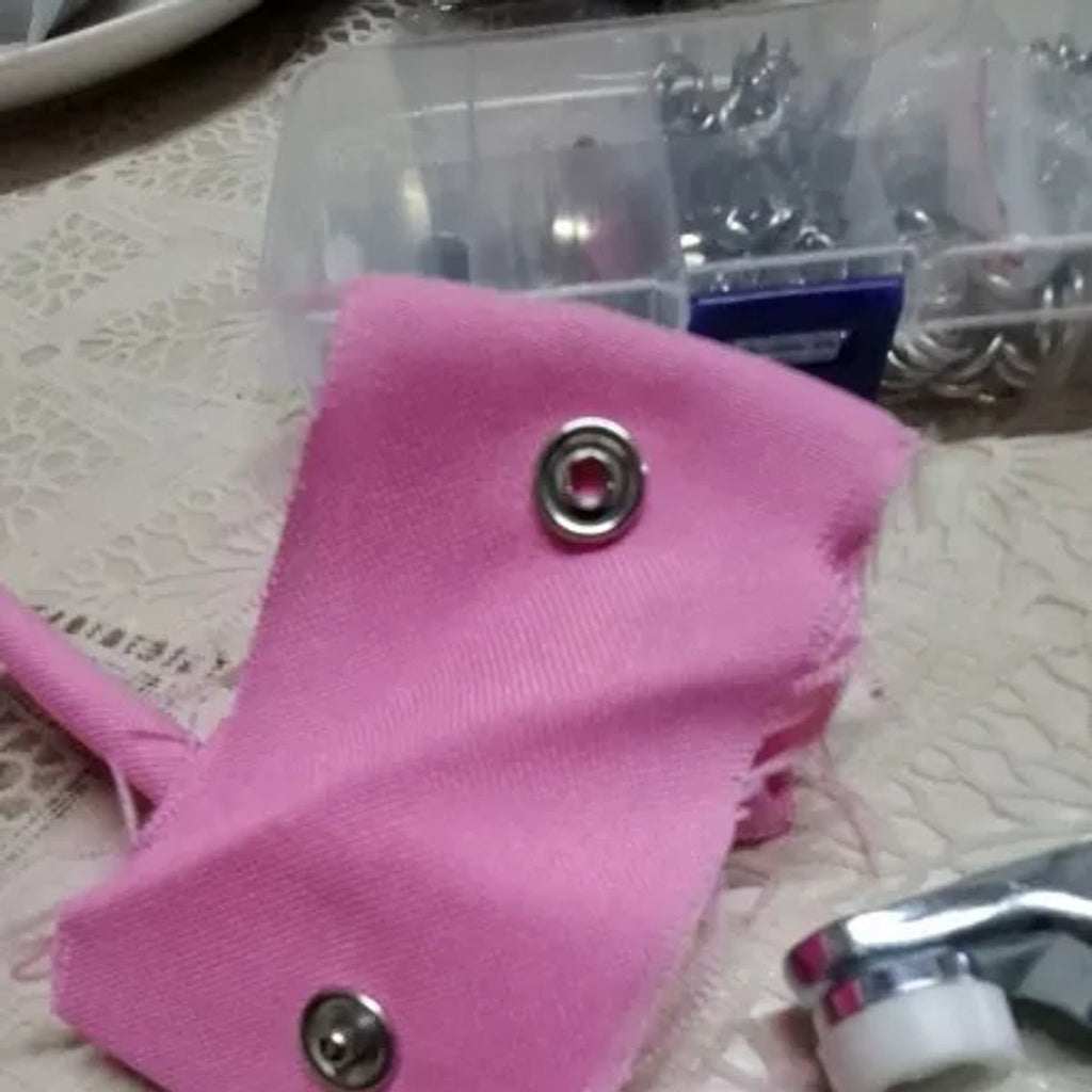 Foto van een koper: close-up van twee drukknopen in roze stof, met de doos op de achtergrond en de bek van de tang onderaan
