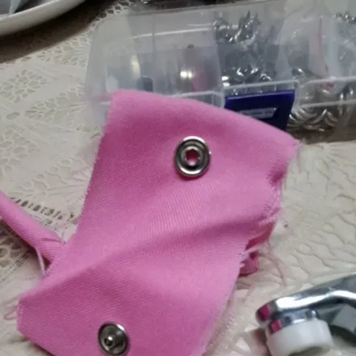 Foto van een koper: close-up van twee drukknopen in roze stof, met de doos op de achtergrond en de bek van de tang onderaan