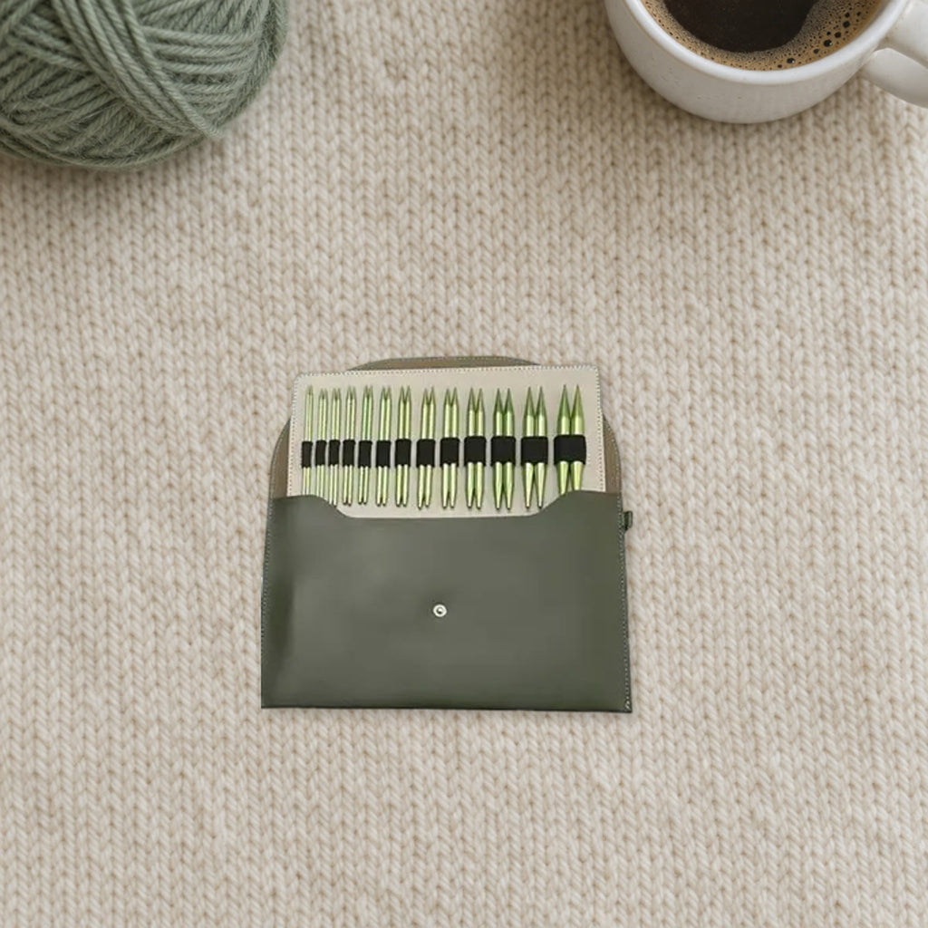 Het open etui met 13 paar groene punten in de houder, op een lichte gebreide wollen plaid naast een bol garen en een kop koffie