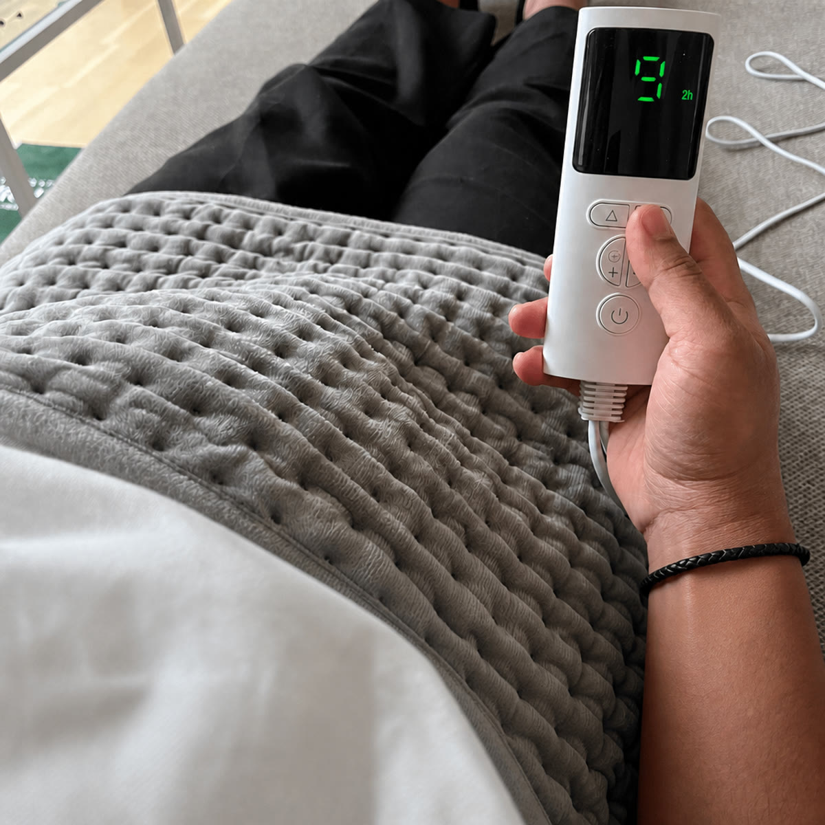 Het warmtekussen van grijze fleece over de dijen, met de bediening op warmtestand 9