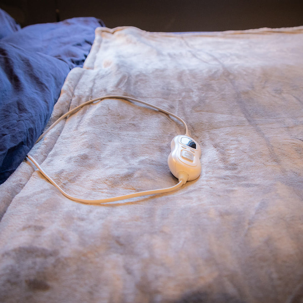 De warmtedeken op bed met de bediening en het snoer erop