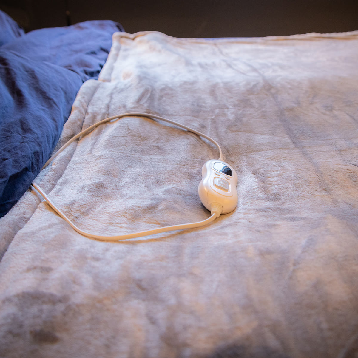 De warmtedeken op bed met de bediening en het snoer erop