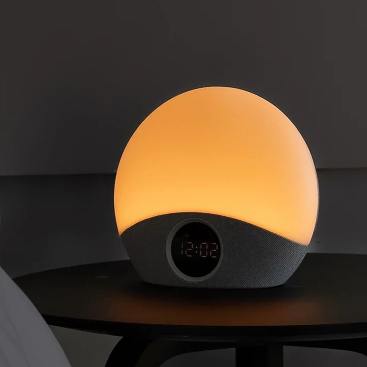 De wekker met licht brandt warmgeel op een nachtkastje en geeft 12:02 aan