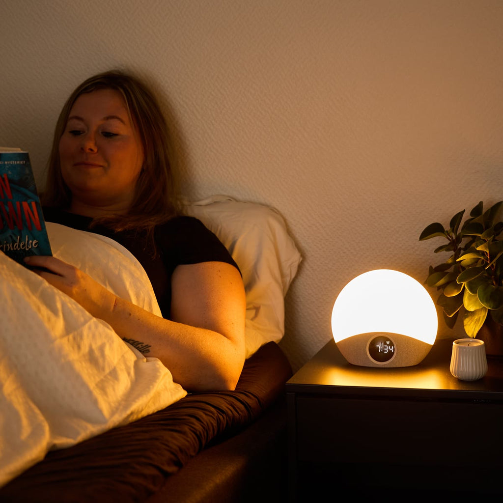 Vrouw leest in bed met de wekker aan als leeslampje op het nachtkastje