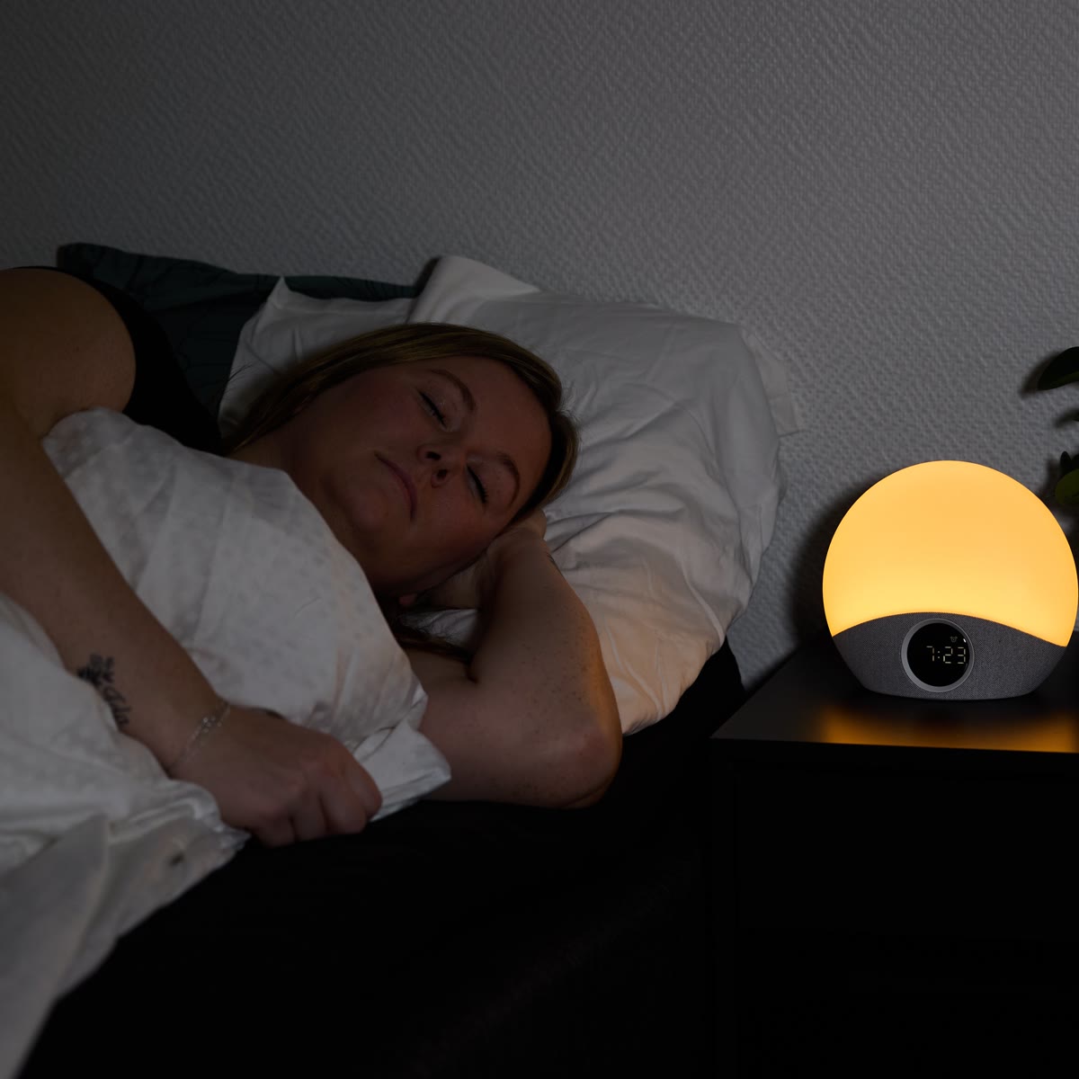Vrouw slaapt naast de wekker, die zwak oranje brandt