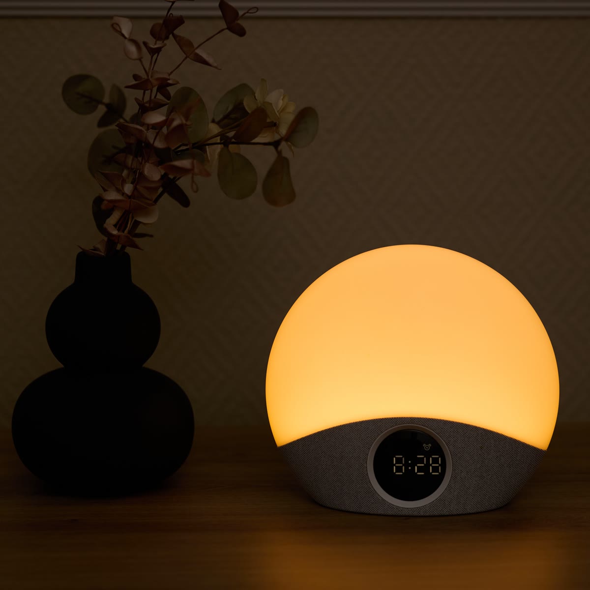 De wekker met warm licht naast een zwarte vaas met eucalyptus