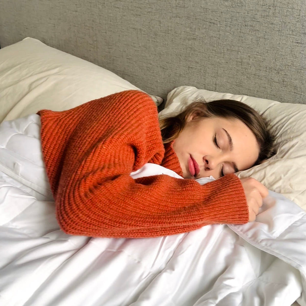 Vrouw in een oranje trui slaapt met de verzwaringsdeken tot aan haar kin