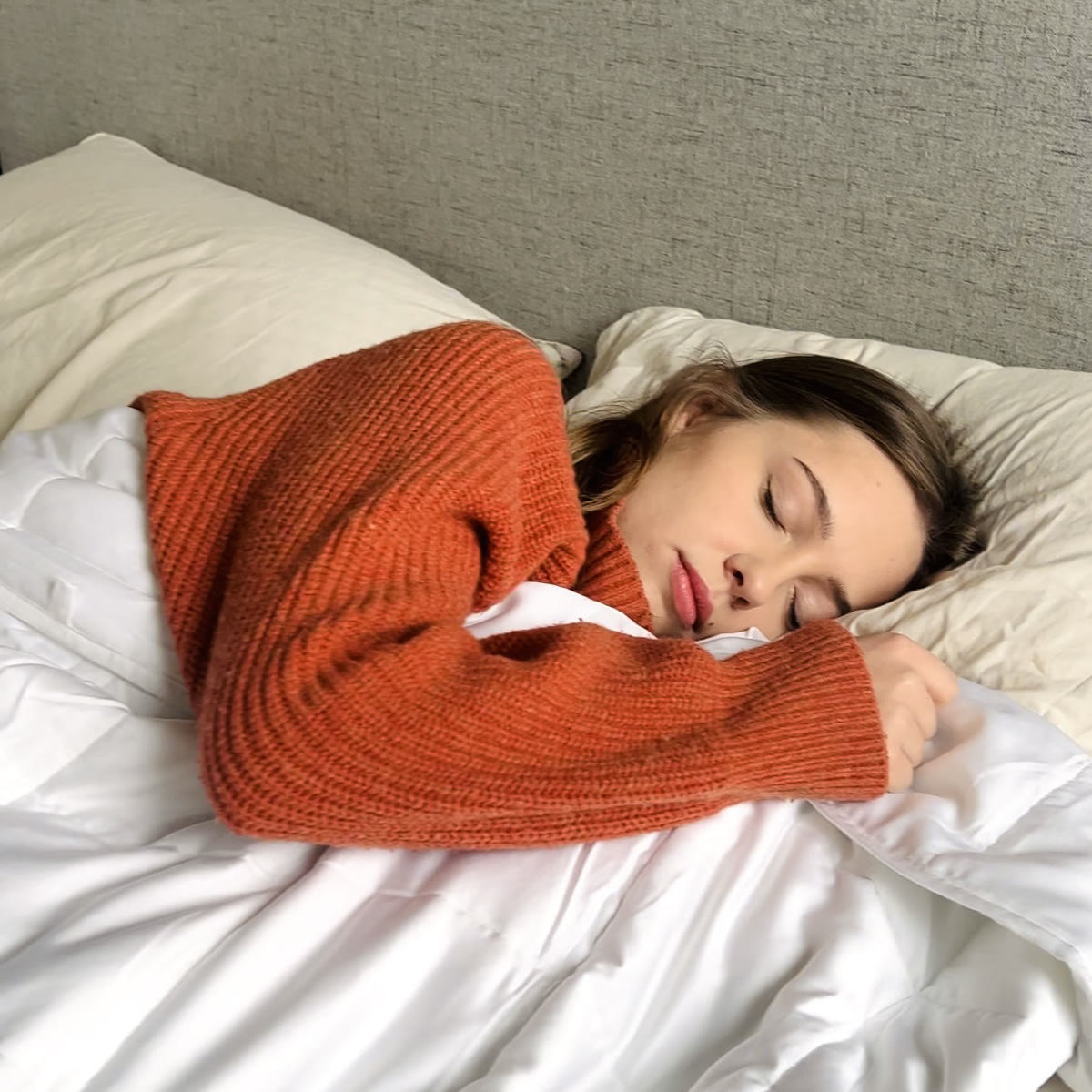 Vrouw in een oranje trui slaapt met de verzwaringsdeken tot aan haar kin