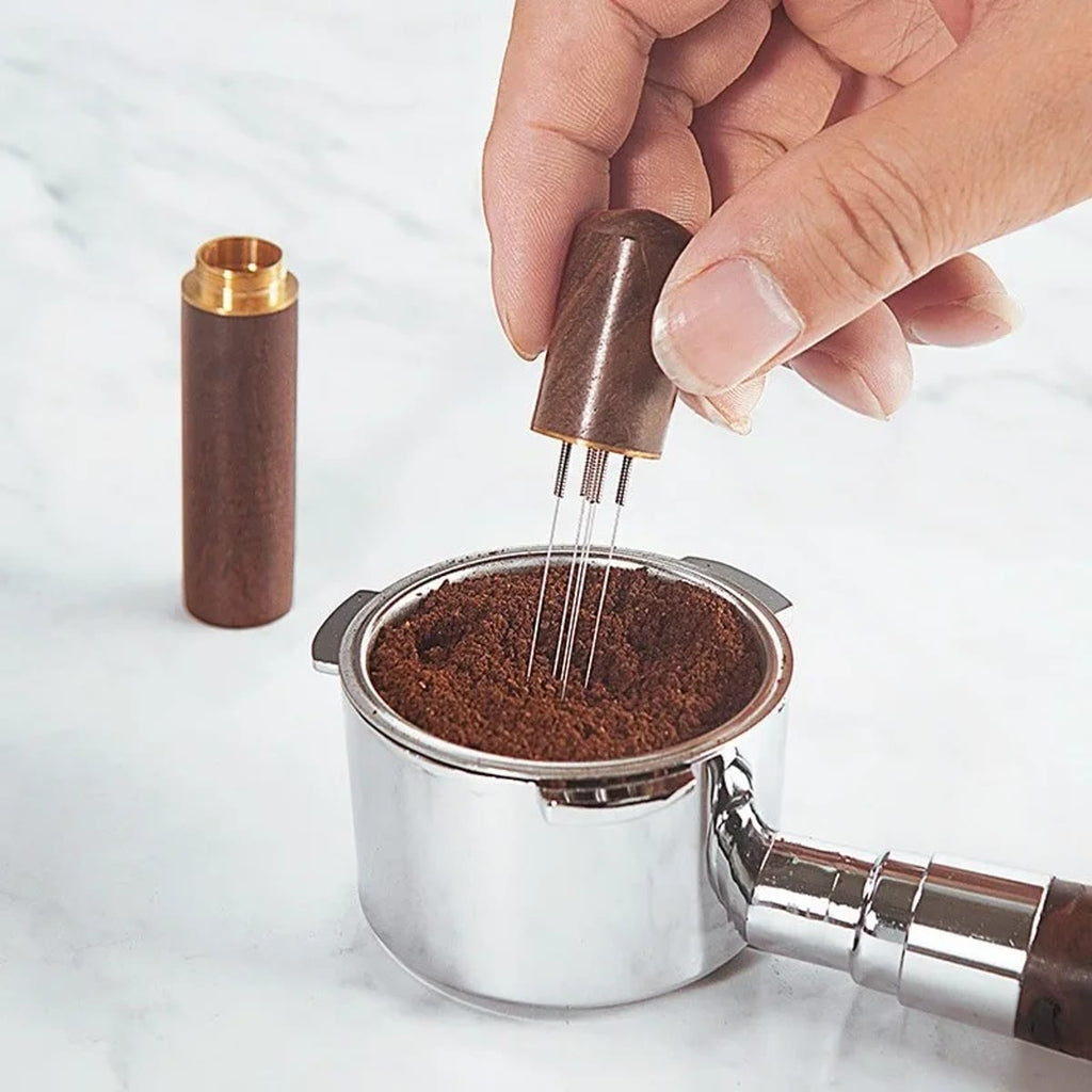 Hand die met de WDT-tool in het koffiepoeder in een filtermand roert, met de dop ernaast