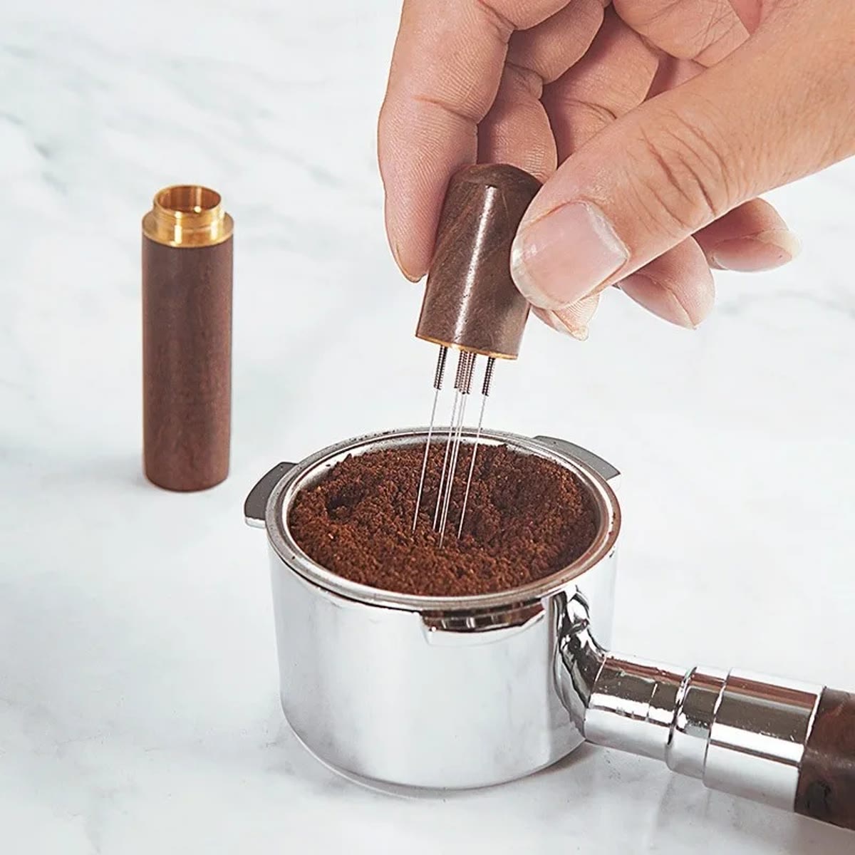 Hand die met de WDT-tool in het koffiepoeder in een filtermand roert, met de dop ernaast