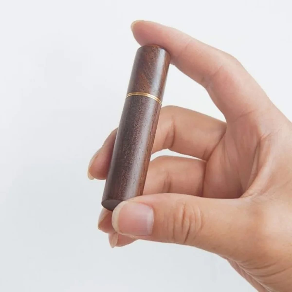 Gesloten houten WDT-tool met goudkleurige ring, tussen twee vingers gehouden