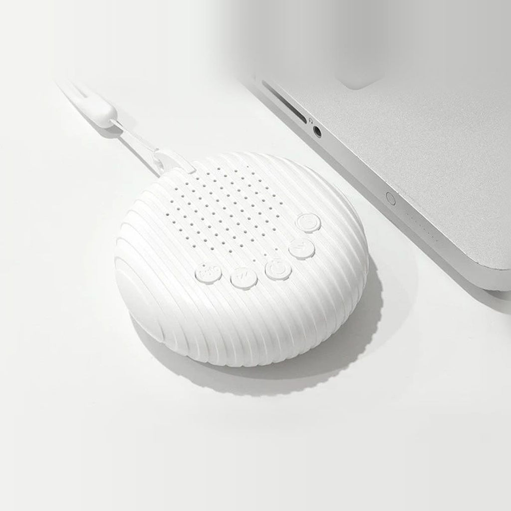 Ronde white noise machine van bovenaf op een wit bureau naast een laptop