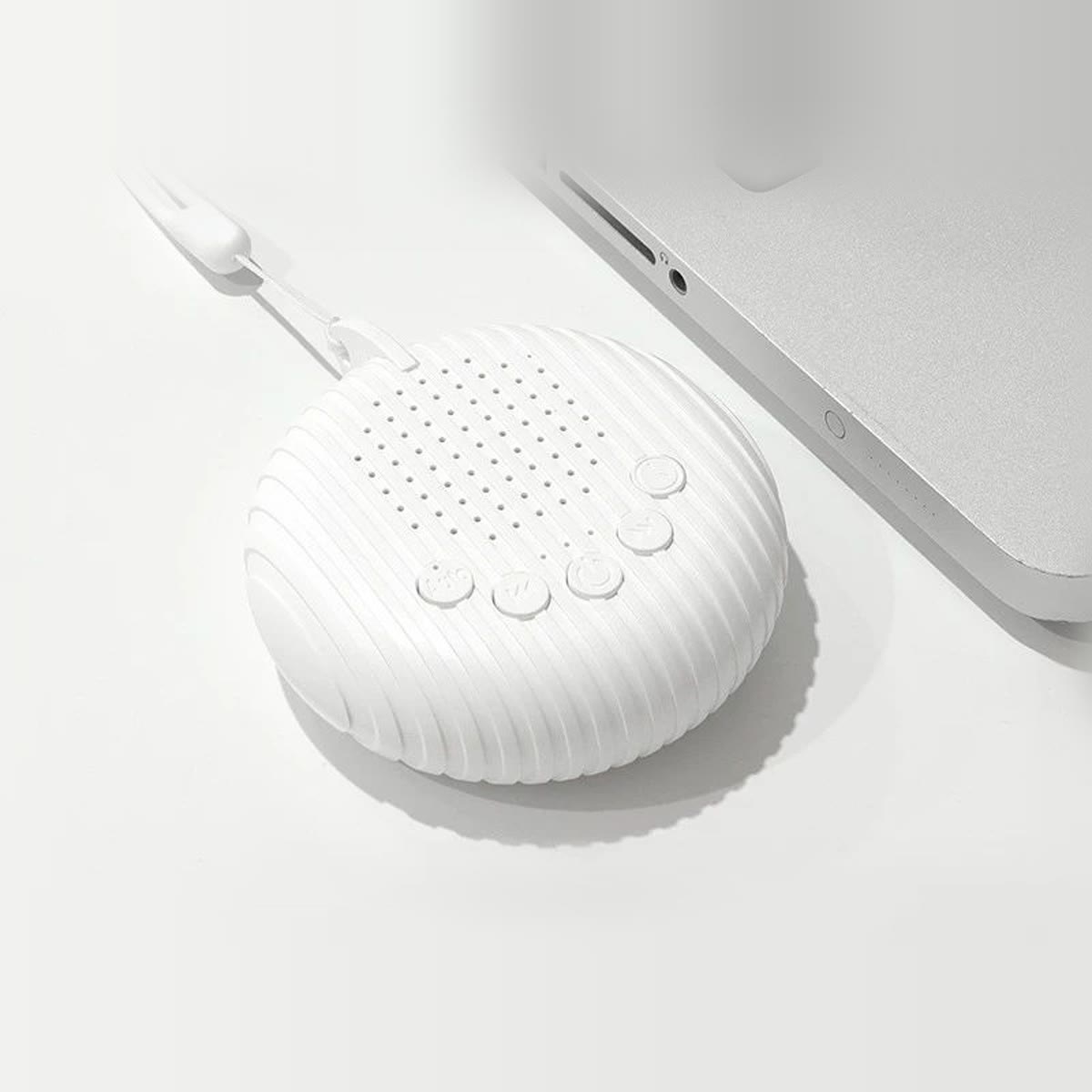 Ronde white noise machine van bovenaf op een wit bureau naast een laptop